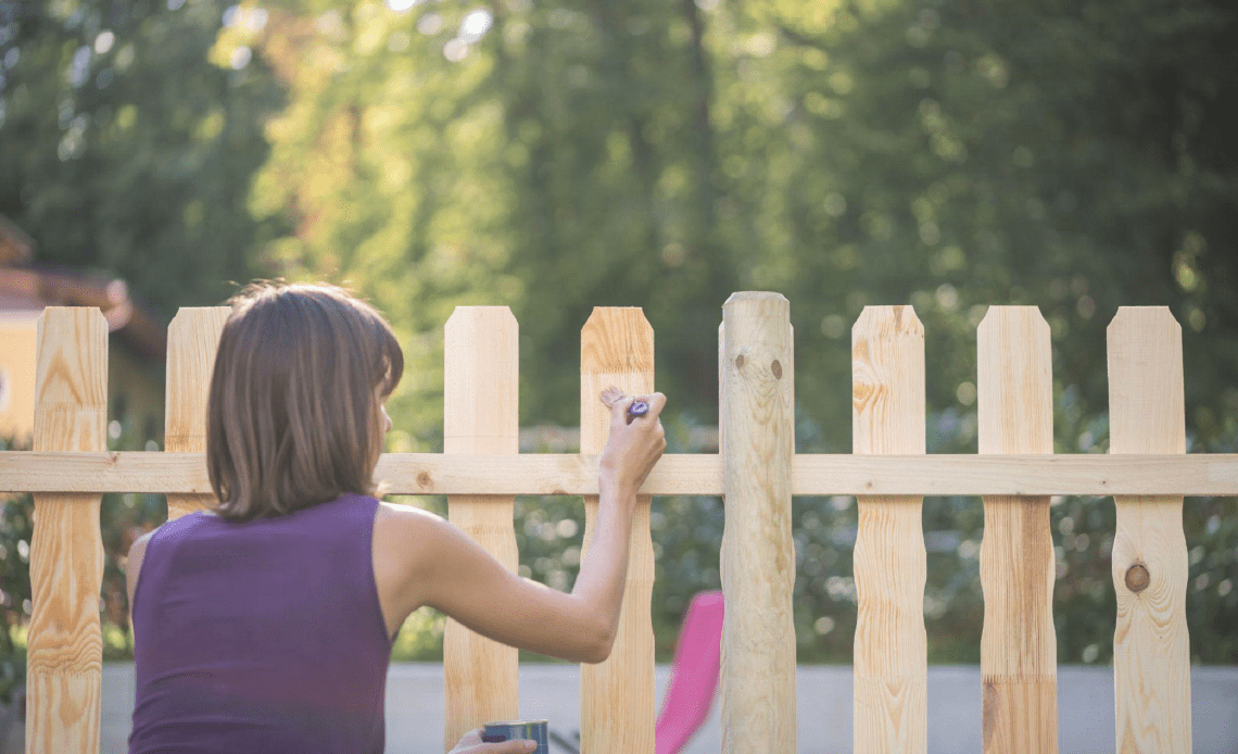 młoda kobieta malująca drewniane ogrodzenie pędzlem